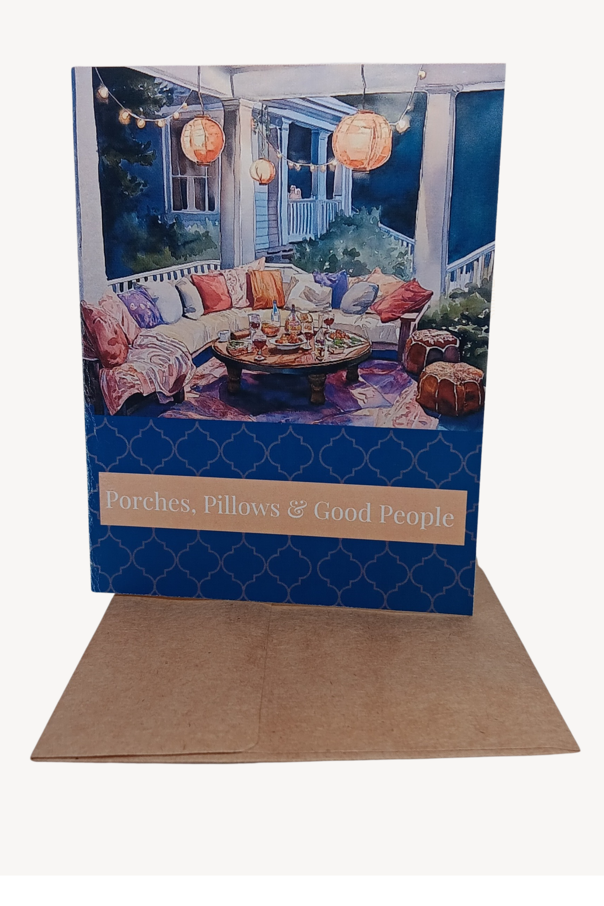 Sophisticated A2 note card featuring watercolor illustration of cozy cushions in a welcoming gathering space. Cover reads 'Porches, Pillows & Good People', with message about cherished moments inside. Deep Sapphire and pearl accent details.
