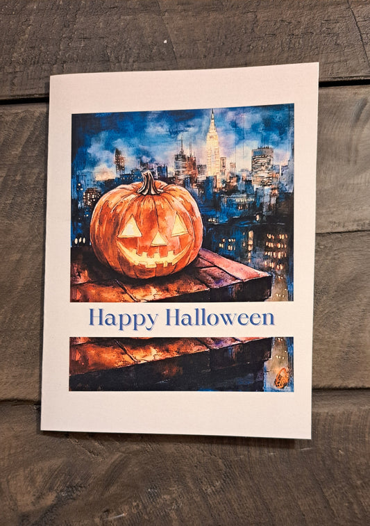 Halloween card with a carved, smiling pumpkin on a rooftop overlooking a city at night, with the message “Happy Halloween”
Image Description: A greeting card showing a carved pumpkin on a rooftop with a cityscape at night. The cover says “Happy Halloween,” and the inside reads “Sending you pumpkin spice wishes and delightful treats.”