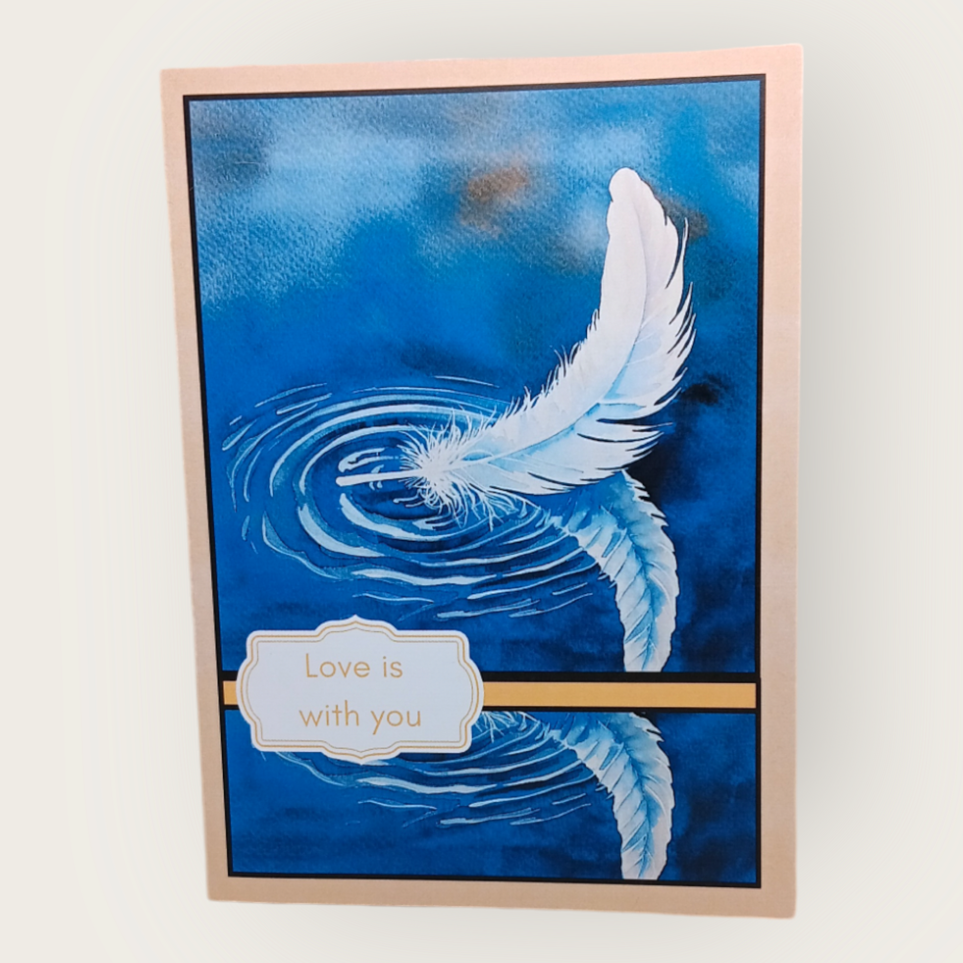 Sympathy card with a white leaf floating on calm blue water, trimmed in beige. The cover reads: “Love is with you.”
Image Description: A serene sympathy card showing a white leaf mirrored on peaceful, sky-blue water. The inside message reads: “In quiet moments, may you find strength in the love that remains.”