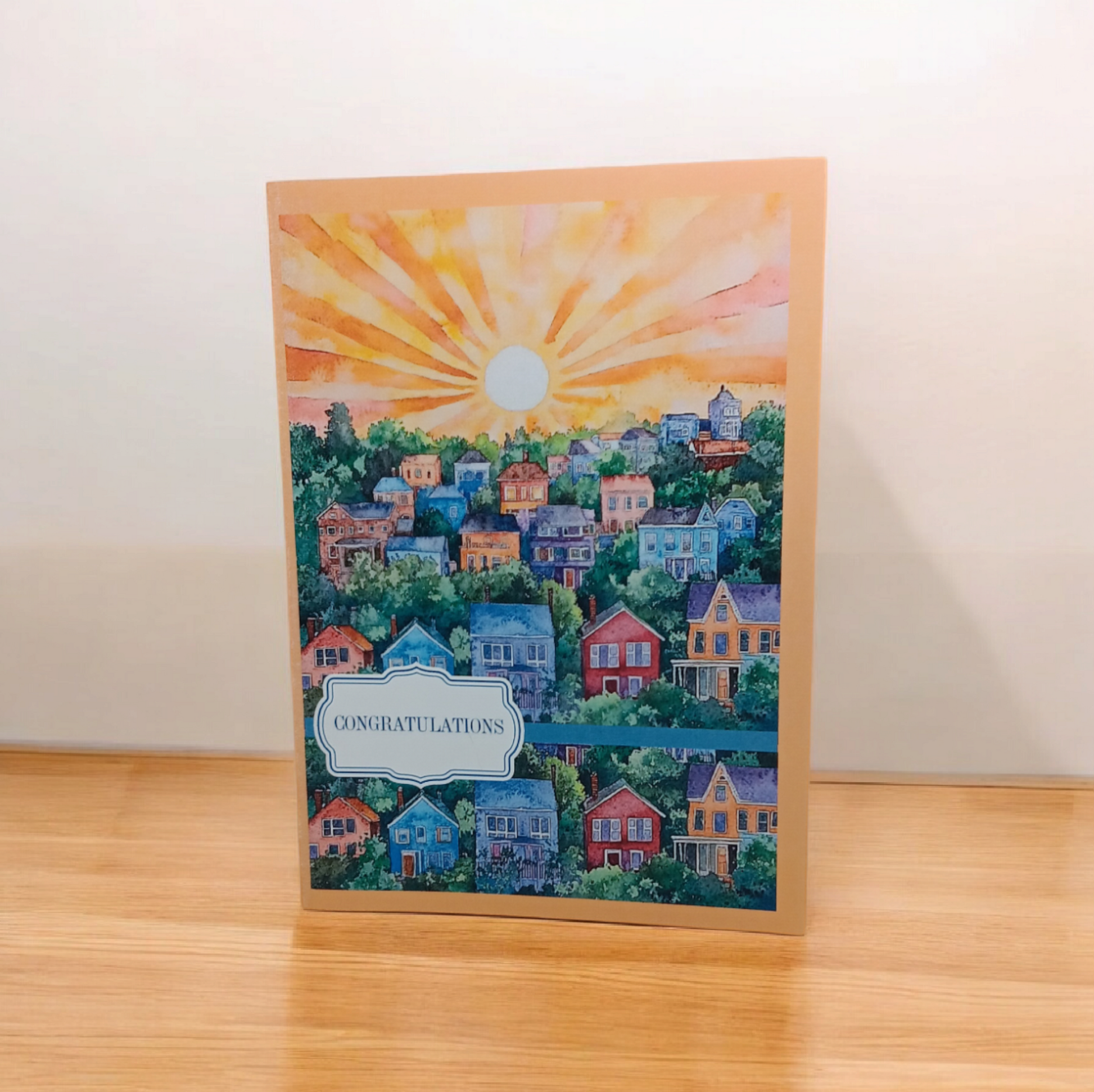 Greeting card featuring a watercolor sunset over a small town, with the message “CONGRATULATIONS.”
Image Description: A greeting card showing a colorful sunset over a town, with “CONGRATULATIONS” on the cover. Inside message reads: “Welcome to your new home! Fill it with love, laughter, and endless joy.”