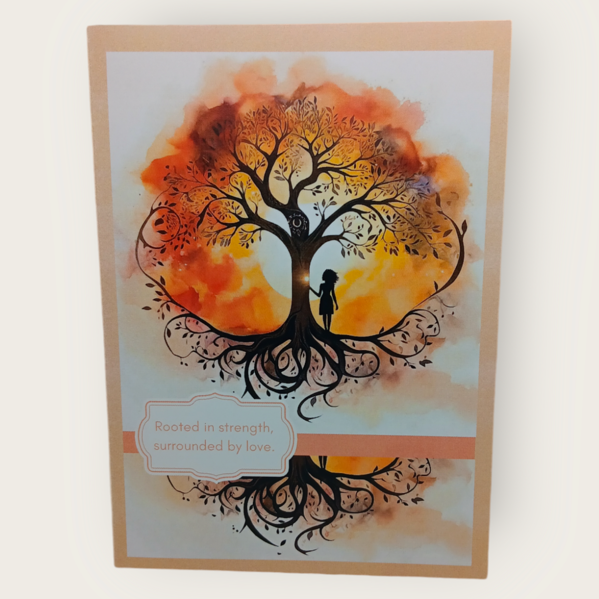 Sympathy card featuring a silhouette of a woman touching a large tree with visible roots, in warm yellow.  golden, and brown tones. The cover reads: ‘Rooted in strength, surrounded by love.  The inside message reads: “May the strengt hand the love around you bring peace. within carry you through."