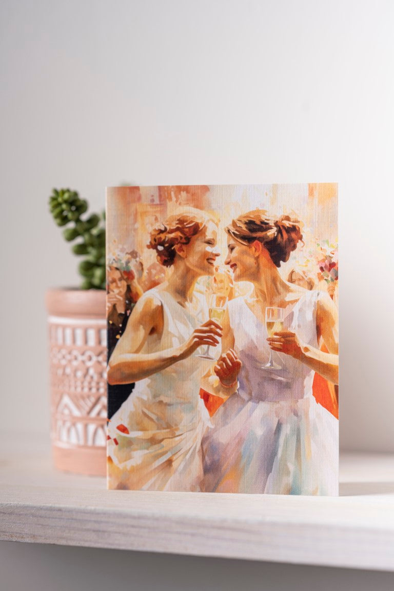 Note card with two brides holding hands and toasting with champagne flutes in vibrant pastel colors.
Image Description: Note card featuring two brides holding hands and toasting with champagne flutes at their wedding, shown in vibrant pastel colors. Printed on linen-textured paper with a blank inside.